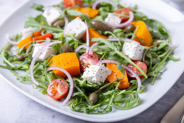 Warm salad with pumpkin, feta cheese, tomatoes, capers, arugula and red onion. Close-up.