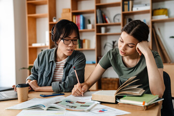 Photo of serious multinational students girls doing homework with laptop