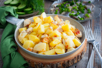 fried potatoes with chicken fillet in a portioned pan on a wooden table, horizontal