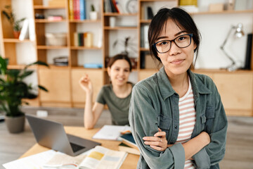 Photo of students girls looking at camera while doing homework with laptop