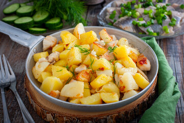 fried potatoes with chicken fillet in a portioned pan on a wooden table, horizontal