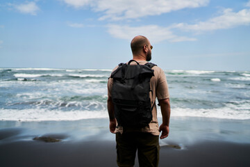 Unrecognizable man with backpack standing on seashore