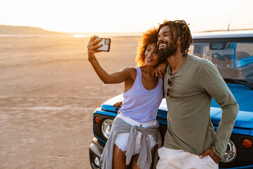 Image of african american couple taking selfie on cellphone in desert