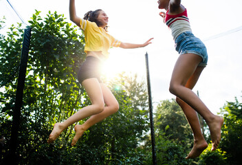 Low angle view of young teenager girls friends outdoors in garden, jumping on trampoline.