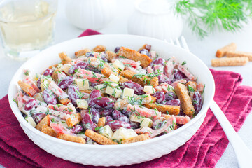 Salad with red beans, smoked sausage, cheese and crackers in a white bowl, horizontal