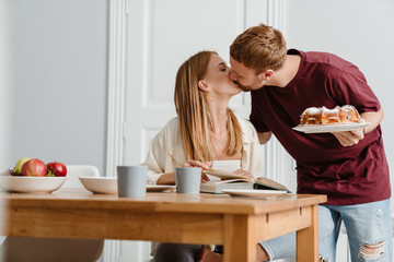 Photo of romantic beautiful couple kissing while drinking tea with pie