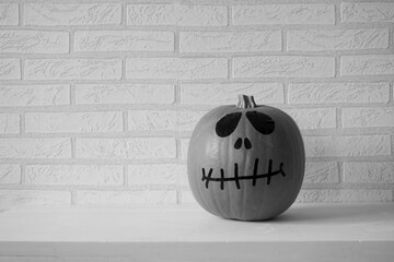 Black and white photograph of a pumpkin with black eyes, nose and mouth, on a white brick background.