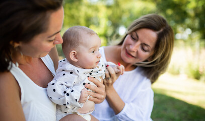 Woman with daughter and baby granddaughter resting outdoors in backyard.