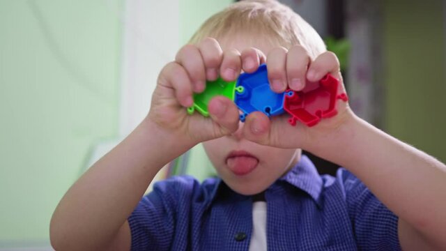 portrait of a disabled boy, child with Down syndrome shows tongue while playing at home close up