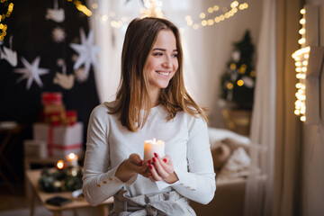 Portrait of young girl indoors at home at Christmas, holding candle.