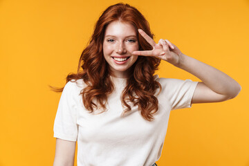 Image of ginger joyful girl winking and gesturing peace sign