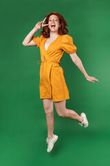 Image of ginger excited girl gesturing peace sign while jumping