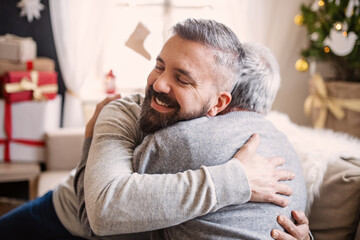 Mature man and senior father indoors at home at Christmas, hugging.