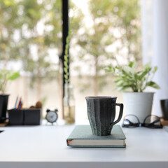 Green old vintage coffee cup with green notebook on white desk decorate with plant pot glasses and clock
