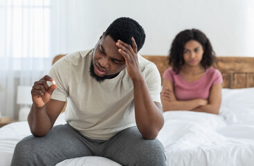 Fototapeta na wymiar Sad black man holding sexual pill, angry girlfriend watching him