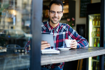 Obraz premium Cheerful man with coffee using tablet