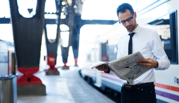 Focused young man reading newspaper on platform of railway station