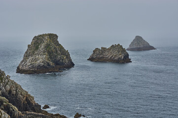 Grey rock formation in the misty atlantic ocean. Rocky islands at the coastline of Brittany, France. Rock formation in the ocean disappears in the fog. Smooth transition between sky and sea.