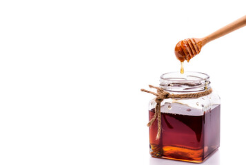 glass jar full of honey and dipper isolated on white background