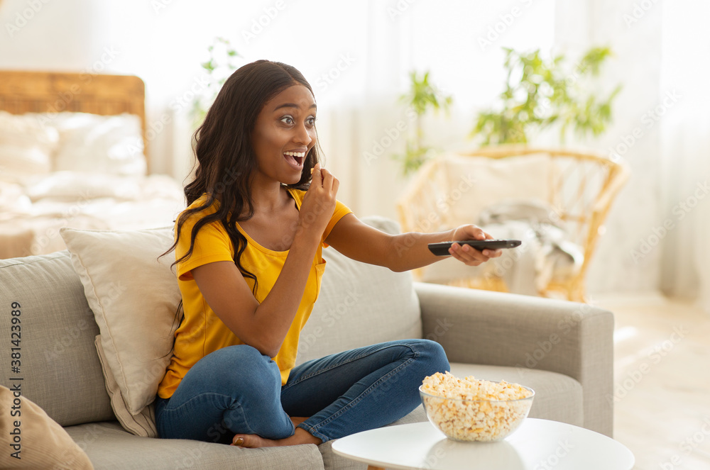 Wall mural pretty african american lady with tv controller enjoying interesting movie at home, blank space