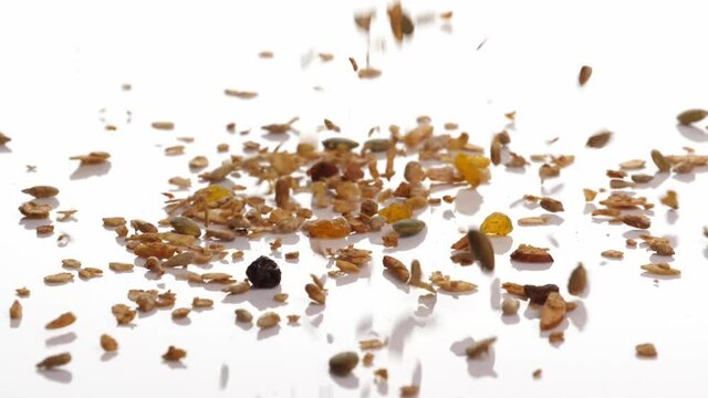Slow motion speed close up scene of granola dropping on floor on white background, muesli texture, pattern of seed scattered falling and bounce on ground, cereal grain for good health, food industrial