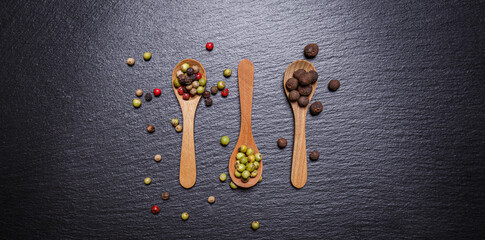 Green pepper, allspice peas and pepper mix in wooden spoons, top view