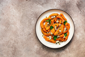 Baked pumpkin slices with herbs and cheese in a plate on a beige grunge background. Top view, flat lay.