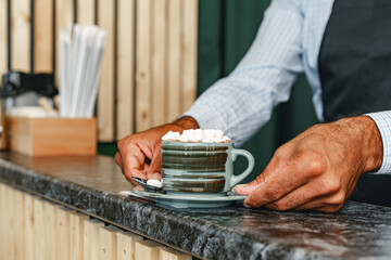Hands of barista serving a cup of hot cocoa drink decorated with marshmellows