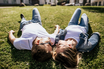 Close up of stylish couple smiling and look at each other lying on green grass. Loving family hold...