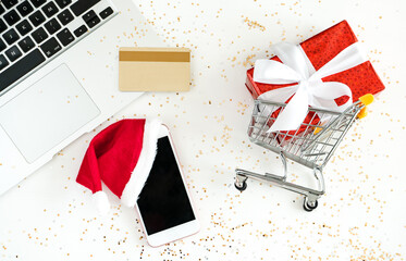 New Year and Christmas online shopping. Mini shopping car, notebook, cellular, credit card and gift box on white background, top view
