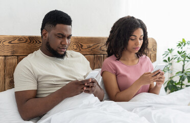 Black man and woman sitting in bed and using their smartphones