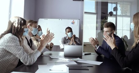 Team of business partners, workers sits in office at conference meeting together, wears protective medical surgical masks on their faces, communicates works in quarantine, applauds celebrates victory - Powered by Adobe