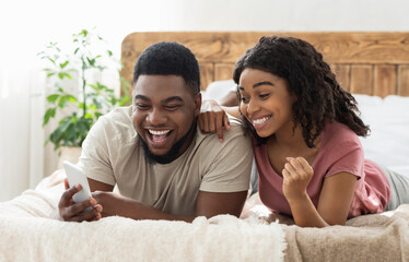 Happy black couple celebrating success, holding smartphone