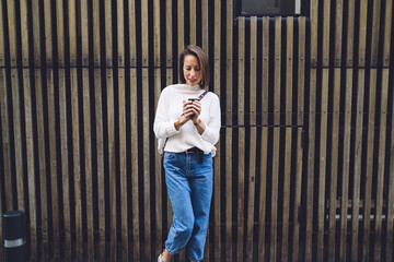 Stylish lady with coffee standing against wooden wall of building