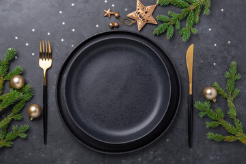 Christmas table setting with empty black ceramic plate, fir tree branch and gold accessories on black stone background. Top view. Copy space - 381431325
