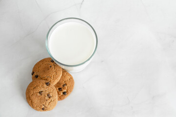 Milk in a glass, next to oatmeal cookies with chocolate chips. White marble background. Selective focus. View from above. Copy space. Banner
