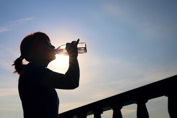 Silhouette of young woman against the background of the morning sky with glare of the sun in the outline, with copy space