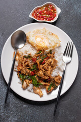 Chicken basil rice with fried egg in white plate on black background. Popular Thai food.