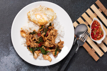 Chicken basil rice with fried egg in white plate on black background.