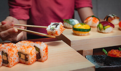 Close up shot of female hand enjoying Japanese cuisine various side dishes by chopstick, tuna uramaki, onigiri sushi set in restaurant