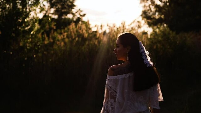 Young brunette woman in a white boho blouse and a ribbon in her hair with a bouquet of dry flowers walking alone in the forest. Early autumn concept. Sunset evening light