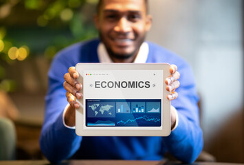 Black Businessman Showing Digital Tablet With Economics Graphs Sitting Indoors