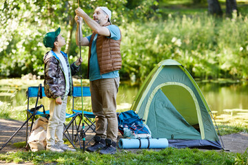 Full length portrait of loving father teaching son to set up fishing equipment while enjoying...