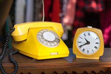 Old yellow clock and yellow telephone with a receiver on a wire and a dial