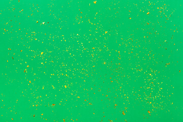 Golden confetti on green paper trendy background. Festive holiday backdrop. Birthday congratulations Christmas New Year. Flat lay, top view, copy space.