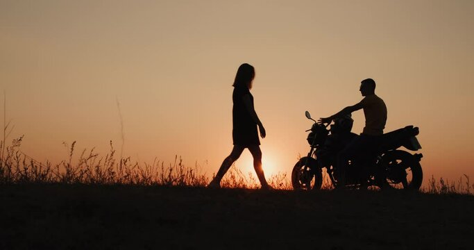 The silhouette of a young woman, goes to the guy who sits on a motorcycle