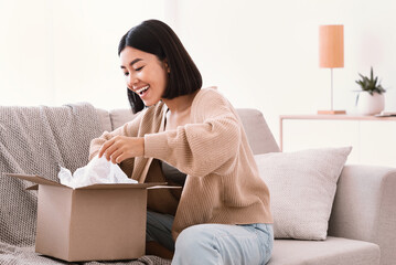 Happy asian lady unpacking parcel after online shopping