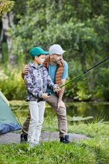 Vertical side view portrait of loving father teaching son fishing while enjoying camping trip together