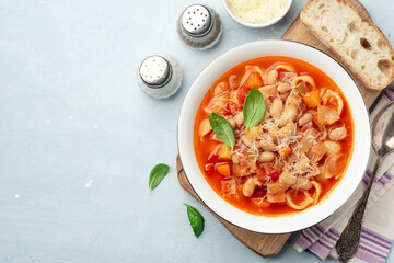 Italian minestrone soup with parmesan cheese and basil on blue concrete background