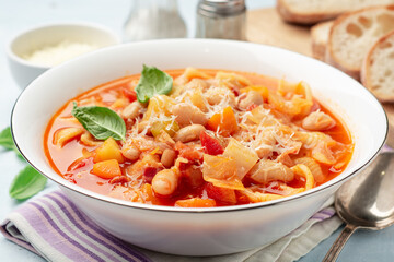 Italian minestrone soup with parmesan cheese and basil on blue concrete background